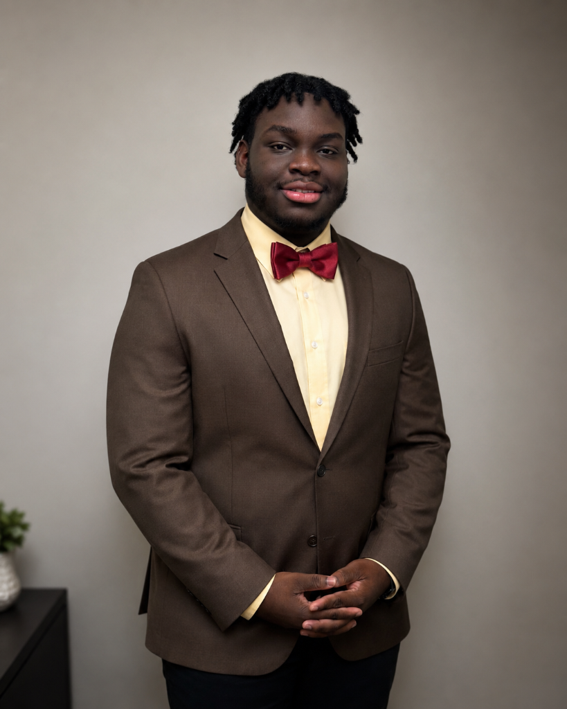 Joel Lewis in a brown suit jacket, butter yellow dress shirt and ruby red bow tie