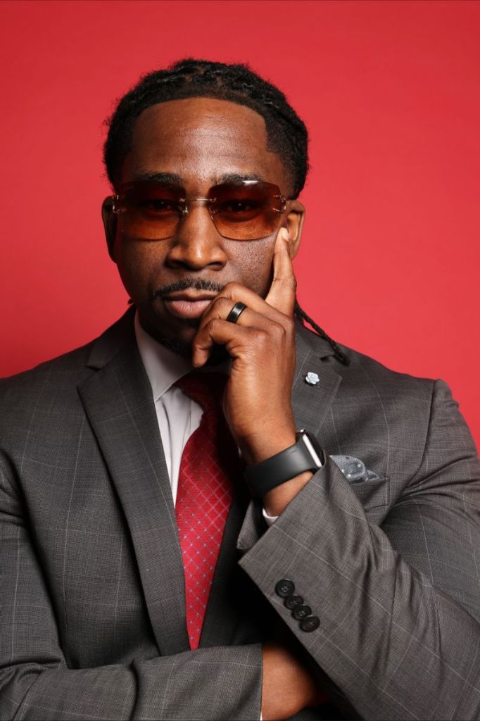 Dr. Victor N. Ukwu, wearing tinted sunglasses, grey suit jacket, white shirt and red necktie with his hand to his face